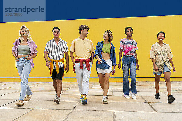 Multiethnische Gruppe junger Freunde  die Seite an Seite vor einer gelben Wand gehen
