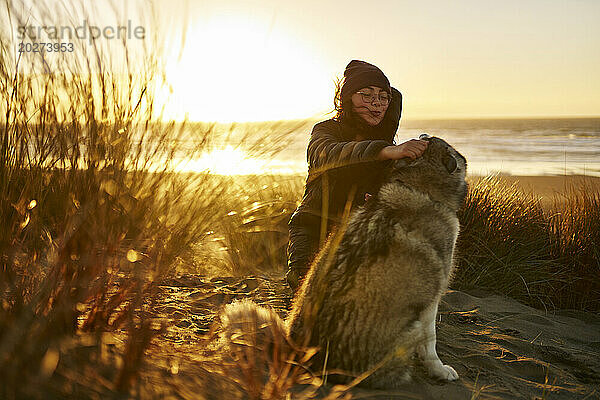 Young woman stroking dog near grass on beach