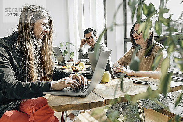 Team von IT-Technikern sitzt am Tisch und programmiert auf Laptops im Büro