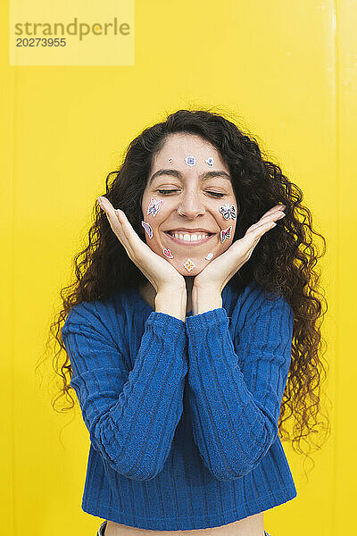 Happy woman smiling with stickers on face against yellow background