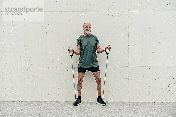 Aktiver älterer Mann trainiert mit Aufhängegurt vor der Wand