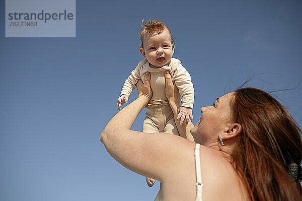 Glückliche Frau hält Tochter unter blauem Himmel