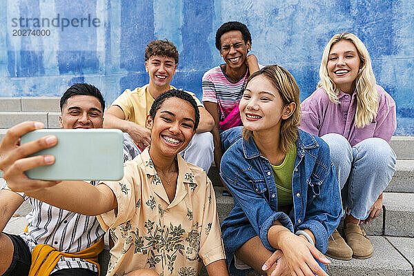 Fröhliche Gruppe junger Leute macht Selfie auf Stufen vor der Wand