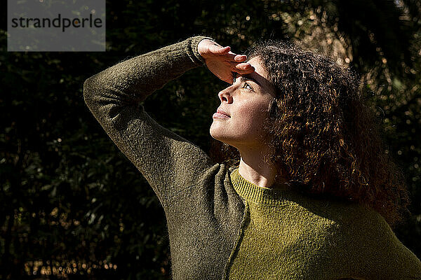 Junge Frau schützt ihre Augen im Park vor Sonnenlicht