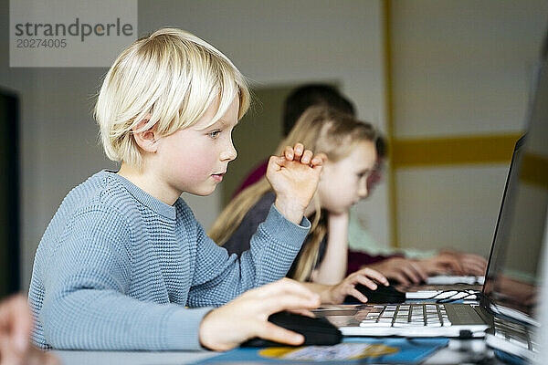 Blond boy learning coding through laptop desk in classroom