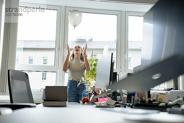 Sorglose Geschäftsfrau  die im Büro mit Luftballons spielt