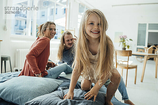 Lächelndes blondes Mädchen mit Mutter und Vater im Hintergrund