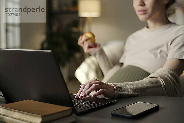 Erwartete Mutter mit Apfel und Laptop im Heimbüro