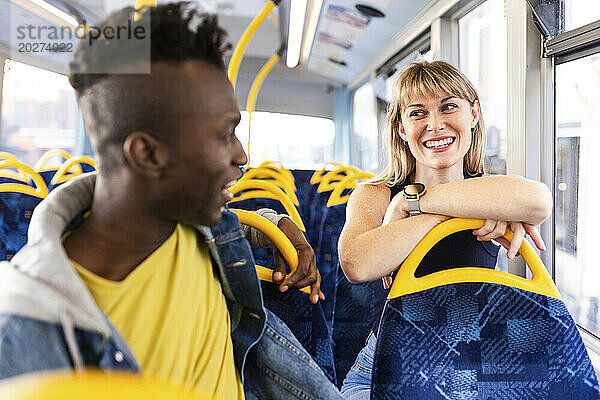 Lächelnde Frau lehnt sich auf den Sitz und unterhält sich mit einer Freundin  die im Bus sitzt