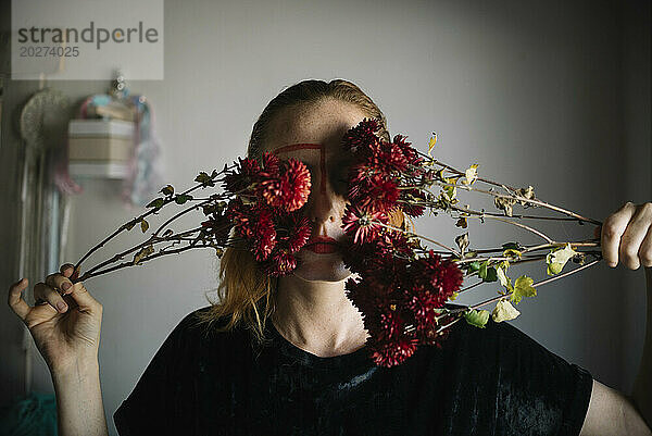 Frau bedeckt Augen mit Blumen vor der Wand