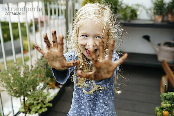 Fröhliches Mädchen zeigt mit Schmutz bedeckte Hände im Balkongarten