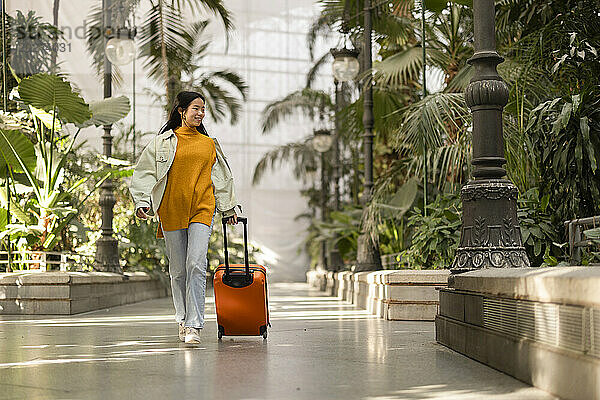 Glückliche junge Frau  die mit Koffer in der Nähe von Pflanzen läuft