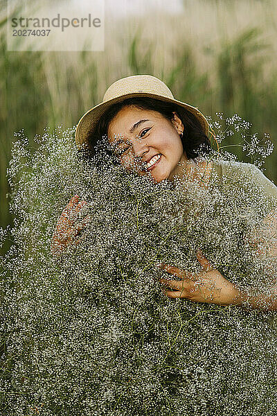 Lächelnde Frau umarmt einen Strauß Schleierkrautblüten auf dem Feld