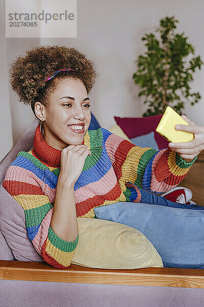 Lächelnde junge Frau macht ein Selfie mit dem Smartphone auf dem Sofa