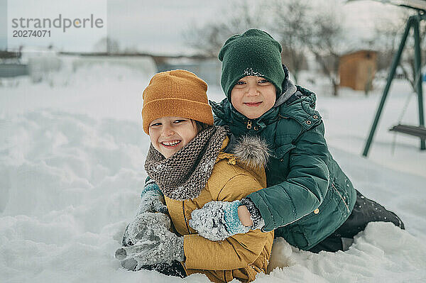 Glückliche Brüder tragen warme Kleidung und spielen im Schnee