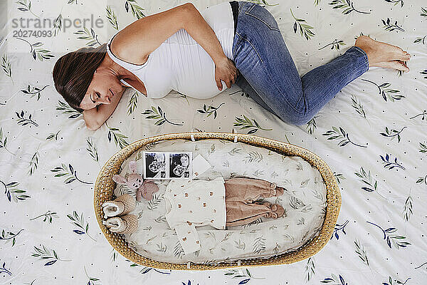 Schwangere Frau liegt zu Hause neben einem Korb im Bett