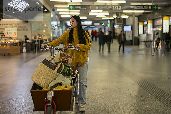 Lächelnde Frau mit Lastenfahrrad am Bahnhof