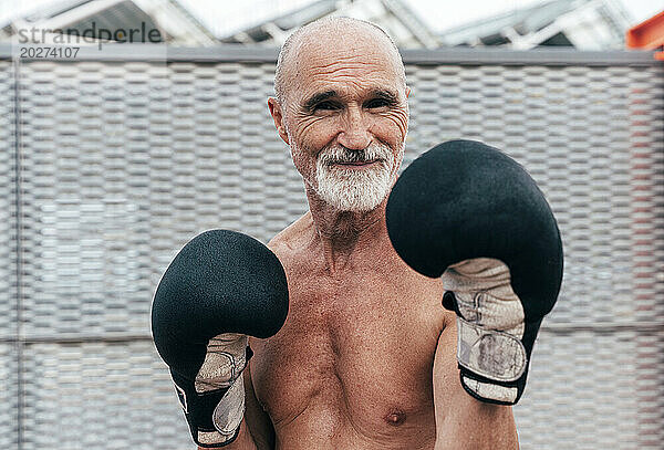 Lächelnder  hemdloser älterer Mann  der mit Boxhandschuhen übt