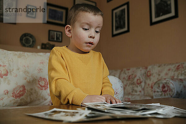 Neugieriger Junge schaut sich zu Hause alte Fotos auf dem Tisch an