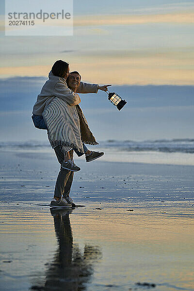 Junger Mann huckepack  Frau mit Laterne am Strand