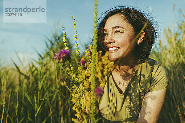 Glückliche Frau mit einem Strauß Wildblumen im Feld an einem sonnigen Tag