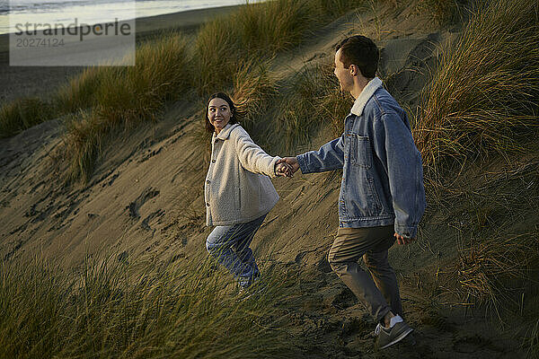 Junge Frau hält die Hand ihres Freundes und geht am Strand spazieren