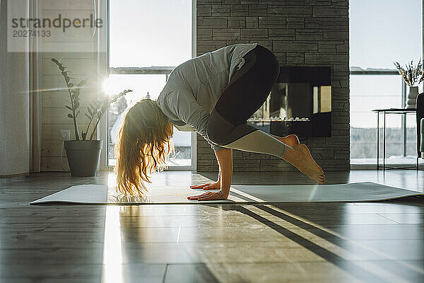 Frau macht Kranich-Yoga-Pose auf Gymnastikmatte zu Hause
