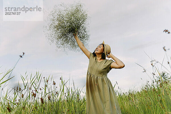 Fröhliche Frau trägt Kleid und hält Schleierkrautblumen auf dem Feld