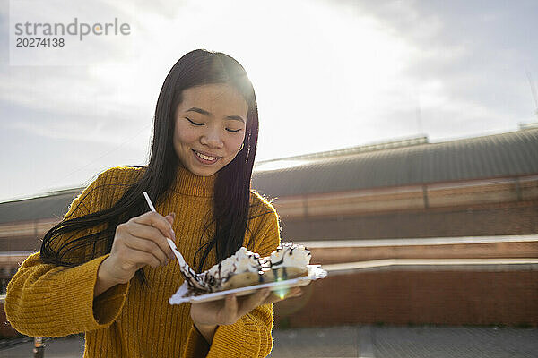 Smiling young woman eating waffle on sunny day