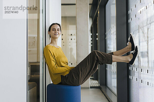 Glückliche junge Geschäftsfrau  die im Bürokorridor sitzt