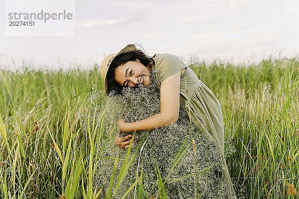 Glückliche Frau umarmt Schleierkrautblüten inmitten von Gras auf dem Feld