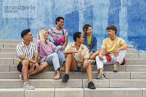 Eine multiethnische Gruppe junger Menschen sitzt auf Stufen vor einer Mauer