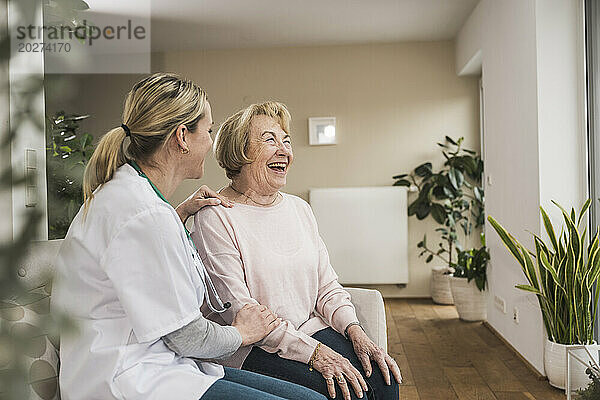 Lächelnder Arzt  der sich um die ältere Frau zu Hause kümmert und ihnen Ratschläge gibt