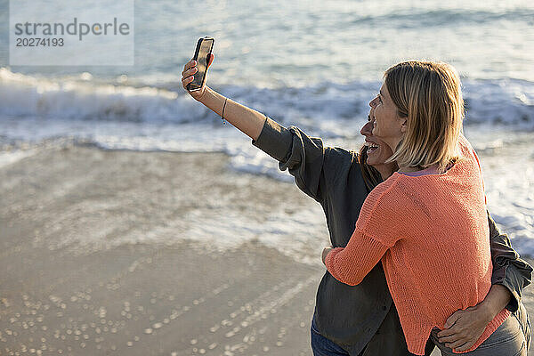 Glückliche Freunde mit ausgestreckten Armen  die am Wochenende ein Selfie am Strand machen