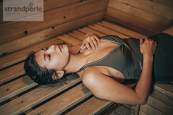 Young woman lying on bench at sauna