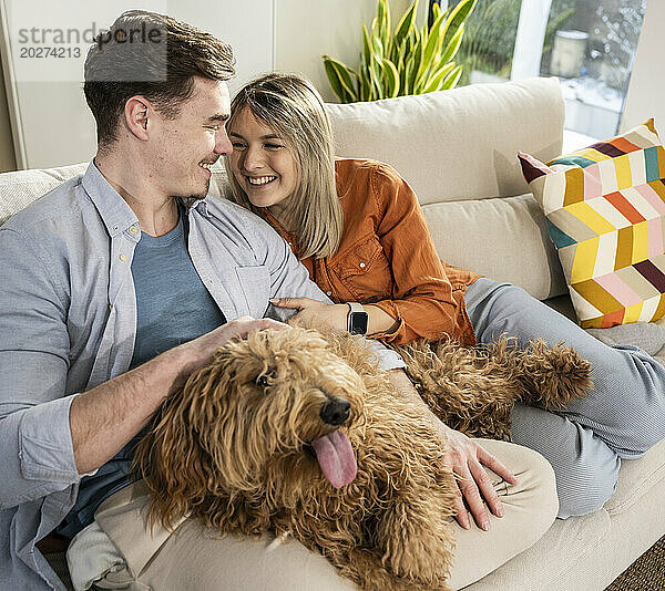 Glückliches junges Paar sitzt mit flauschigem Hund zu Hause auf dem Sofa