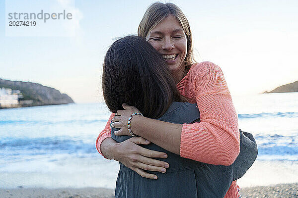Glückliche Frau umarmt Freundin am Strand