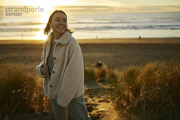 Lächelnde junge Frau am Meeresstrand bei Sonnenuntergang