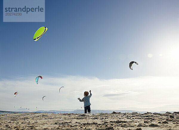 Boy playing and watching kite surfers at beach