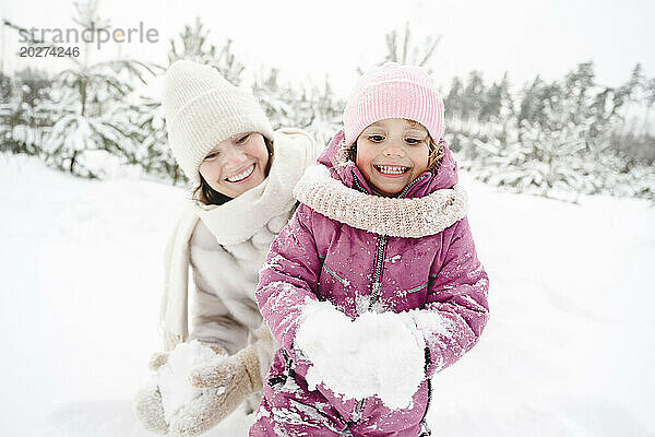 Glückliche Mutter und Tochter spielen im Winterpark mit Schnee