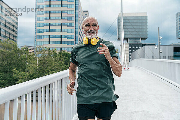 Lächelnder  aktiver älterer Mann  der auf der Fußgängerbrücke läuft