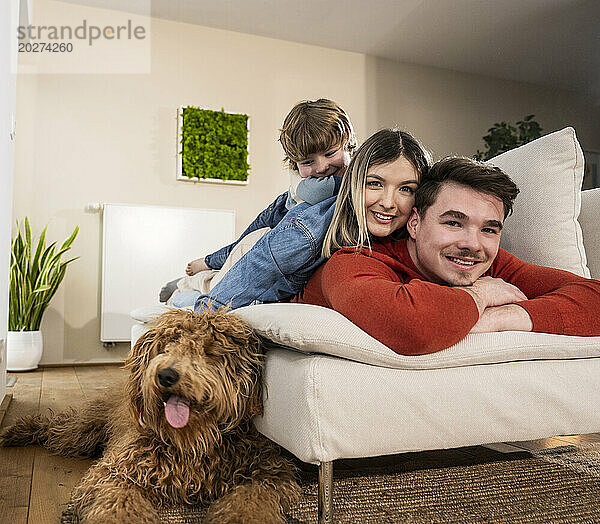 Smiling family lying on sofa near dog at home