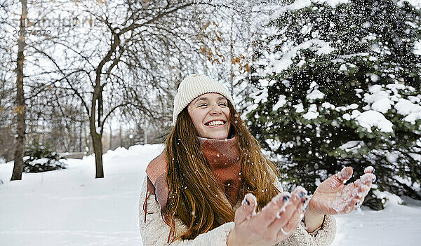 Fröhliche Frau spielt im Winterpark mit Schnee