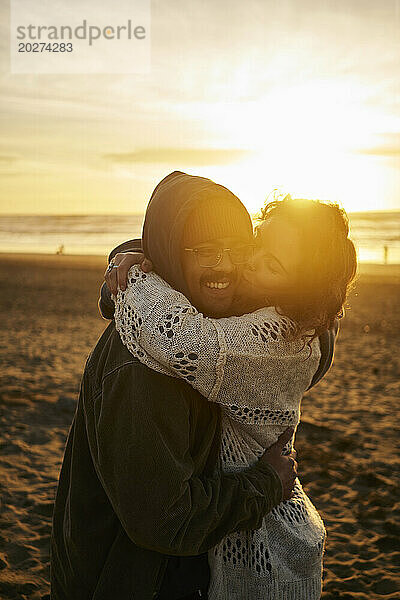 Frau küsst lächelnden Mann am Strand