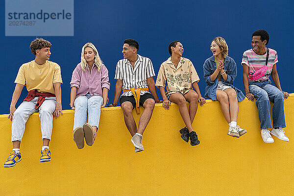Fröhliche Freunde mit bunter Kleidung sitzen zusammen an einer gelben Wand