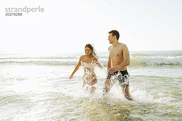 Glückliches Paar  das am Strand im Wasser spielt