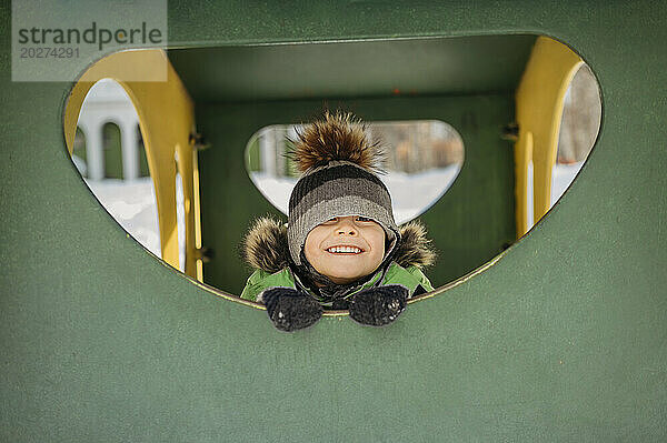 Smiling boy in warm clothes playing in playground