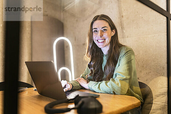 Glückliche reife Geschäftsfrau sitzt mit Laptop im Büro