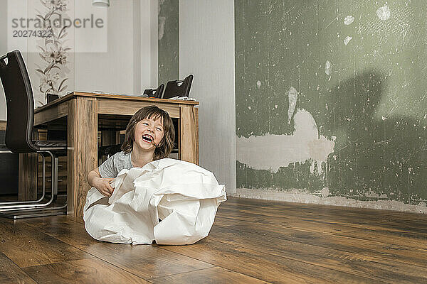 Playful boy wrapped in white wallpaper having fun at home