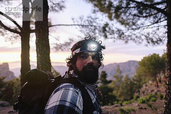 Man wearing headlamp near trees in front of mountains